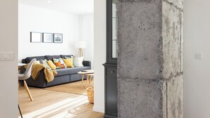 Un soggiorno moderno con un divano grigio, cuscini colorati, un tavolino in legno e un pilastro in cemento.