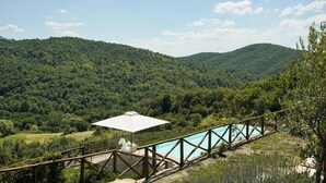 Ein Poolbereich mit Holzterrasse und weißem Sonnenschirm, umgeben von einem Metallzaun.