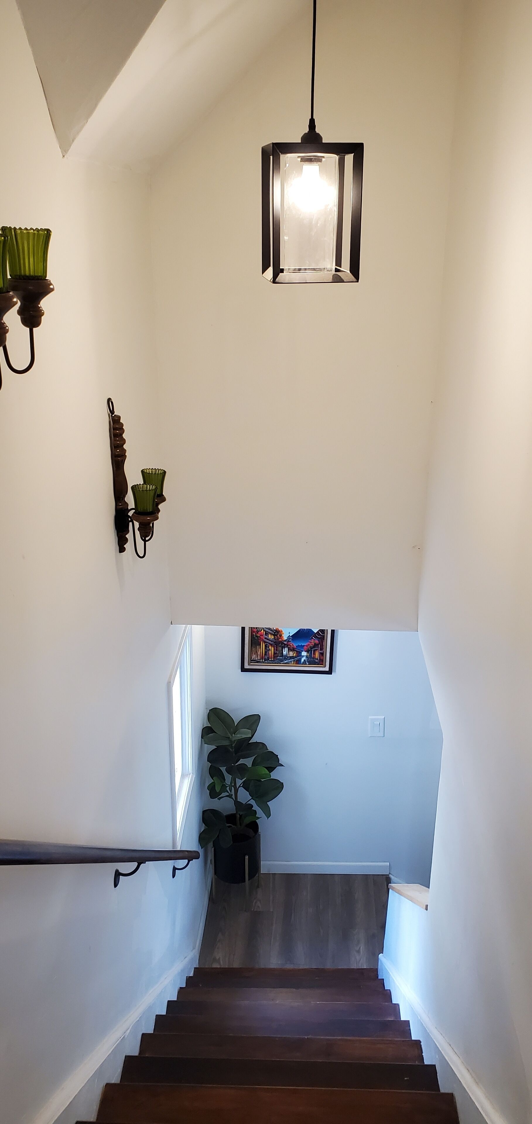 Una escalera con escalones de madera, una lámpara colgante, apliques de pared y un cuadro enmarcado.