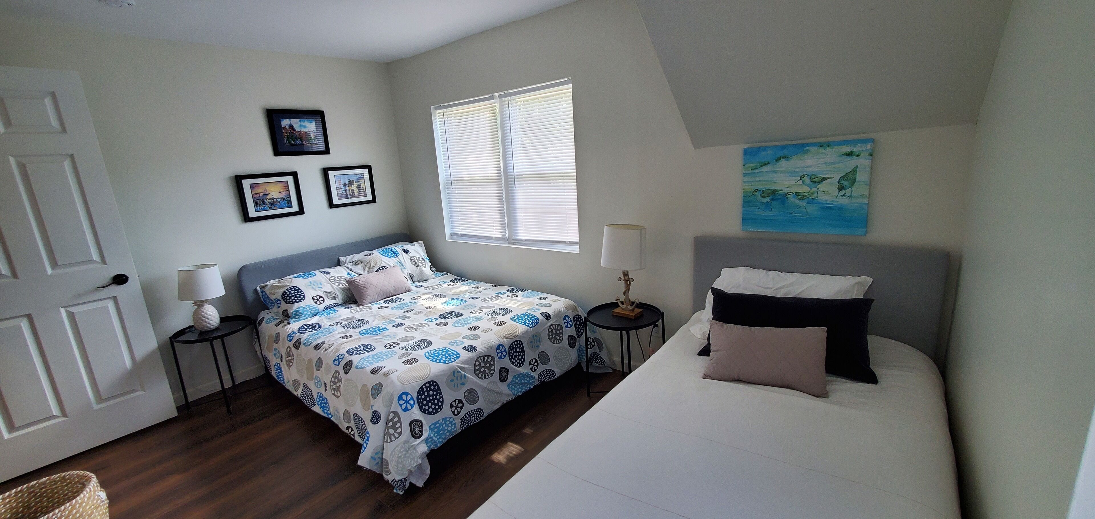 Un dormitorio con cama, mesitas de noche, lámpara, ventana con persianas y decoración en la pared.