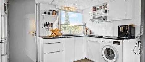 A compact kitchen with white cabinetry, a built-in washing machine, and a window providing natural light.