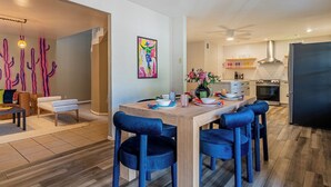 Una sala de estar moderna con una mesa de comedor de madera, sillas de terciopelo azul y un cuadro abstracto colorido.