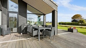 An outdoor patio with a dining table and chairs, a grill, and a view of a residential area. - Cozy home in Sæby with house sea view (Sæby)