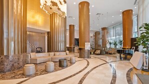 A spacious lobby with a curved marble floor, a seating area with sofas and ottomans, tall decorative columns, and a reception desk. - 1910 International  Resort Deluxe 2 Queen  Ocean Front (Sunny Isles Beach)