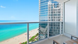 A balcony with a view of a beach and a modern building. - 1910 International  Resort Deluxe 2 Queen  Ocean Front (Sunny Isles Beach)