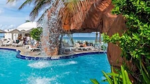 A pool with a waterfall feature surrounded by lounge chairs and a rocky landscape. - 1910 International  Resort Deluxe 2 Queen  Ocean Front (Sunny Isles Beach)