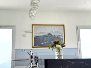 A modern kitchen with a marble countertop, a stainless steel faucet, and a crystal chandelier.