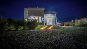 Una casa moderna con una entrada iluminada, un camino de acceso y un vehículo estacionado cerca.