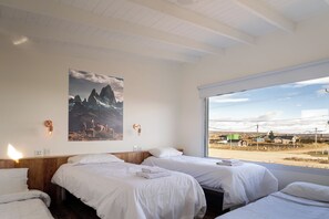 Ein Hotelzimmer mit zwei Betten, einem Gemälde von einer Berglandschaft und Blick auf eine Stadt durch ein großes Fenster.