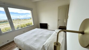 Un dormitorio con una ventana grande, una cama, una mesita de noche y un espejo.