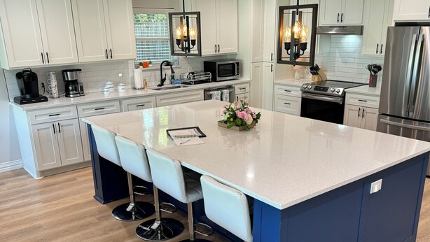 A modern kitchen with a central island, bar stools, stainless steel appliances, and a farmhouse chandelier.