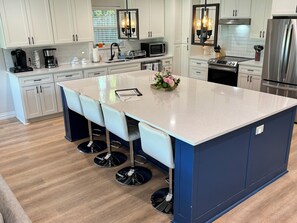 Una cocina moderna con una isla central, taburetes de bar, electrodomésticos de acero inoxidable y una lámpara estilo campestre.