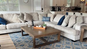 A living room with a sofa set, coffee table, and a kitchen area in the background.