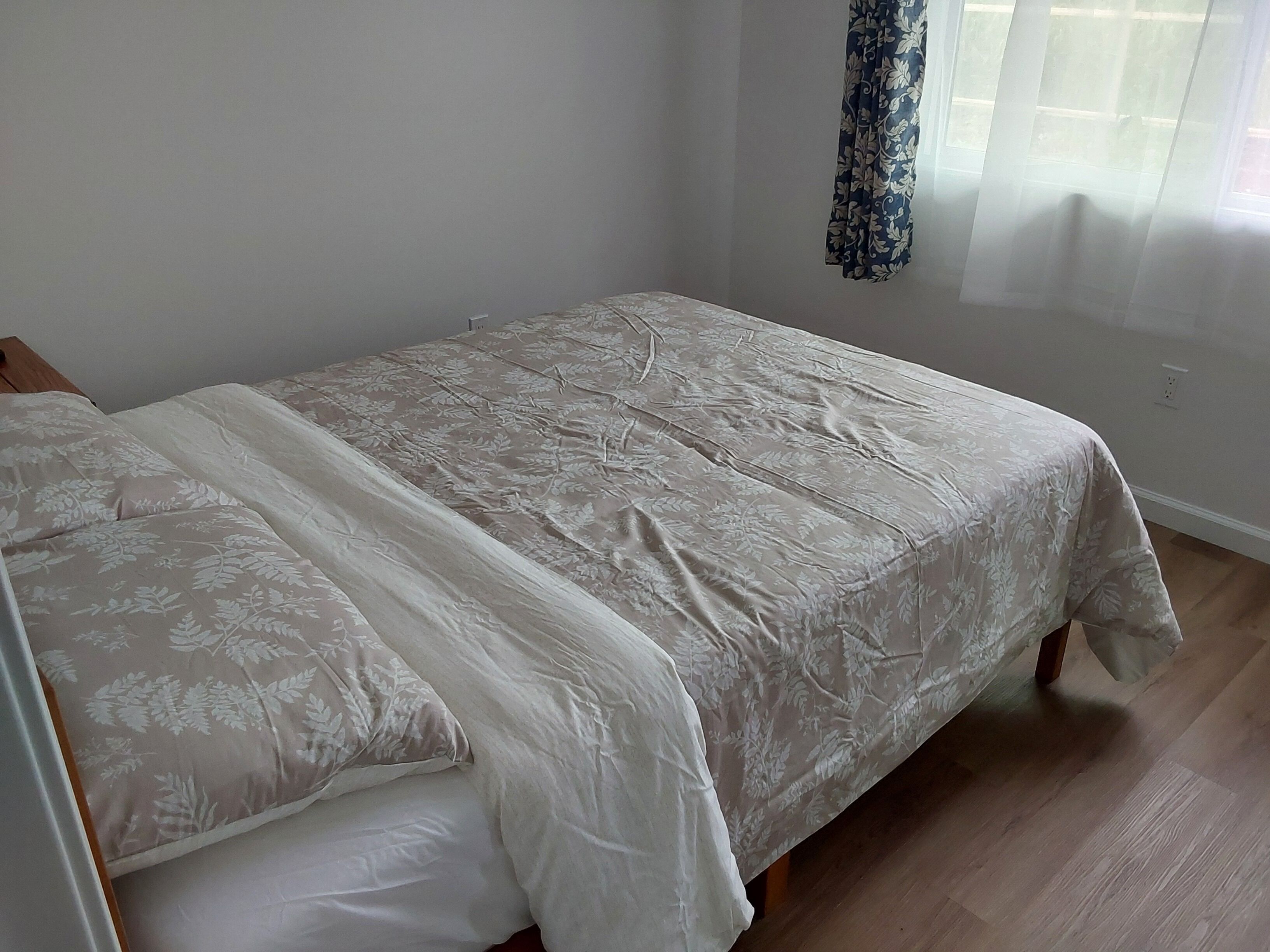 A single bed with a floral bedspread and matching pillows in a room with wooden flooring and a plain wall.