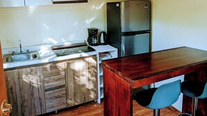 Una cocina con armarios de madera, un refrigerador de acero inoxidable, una mesa de comedor de madera con dos taburetes de bar y una lámpara colgante.