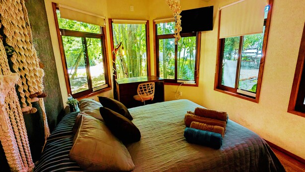 Un dormitorio con cama, almohadas, una silla y un televisor.