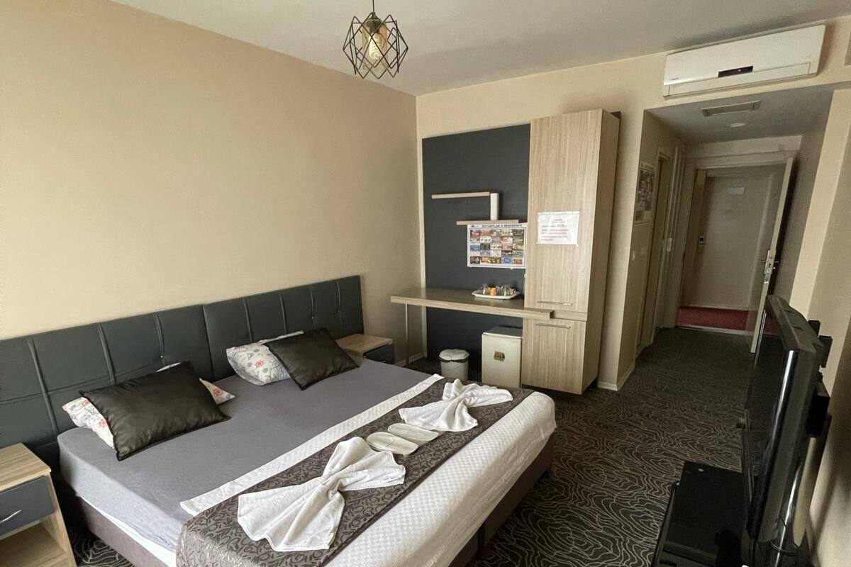 A hotel room with a large bed, a desk, a TV, and a patterned carpet.