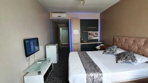 Ein Hotelzimmer mit einem Bett, einem Schreibtisch mit Computer, einem Fernseher und einem Kühlschrank.