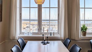 Een eetgedeelte met een tafel en stoelen, uitzicht op een haven met boten, en een hangende lamp.