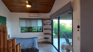 A room with a bamboo wall, a bed, a window with a view of greenery, and a sliding glass door leading outside.
