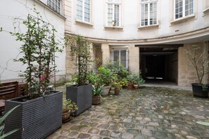 A courtyard with stone paving, potted plants, and a wooden bench. - Studio Temple - Welkeys (Paris)