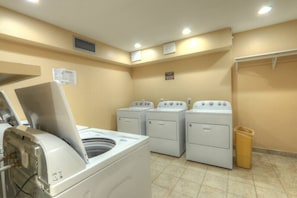 Una sala de lavandería con cuatro lavadoras, un secador y un cubo de basura.