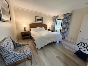 Un dormitorio con cama, mesitas de noche, una silla y una ventana con cortinas.