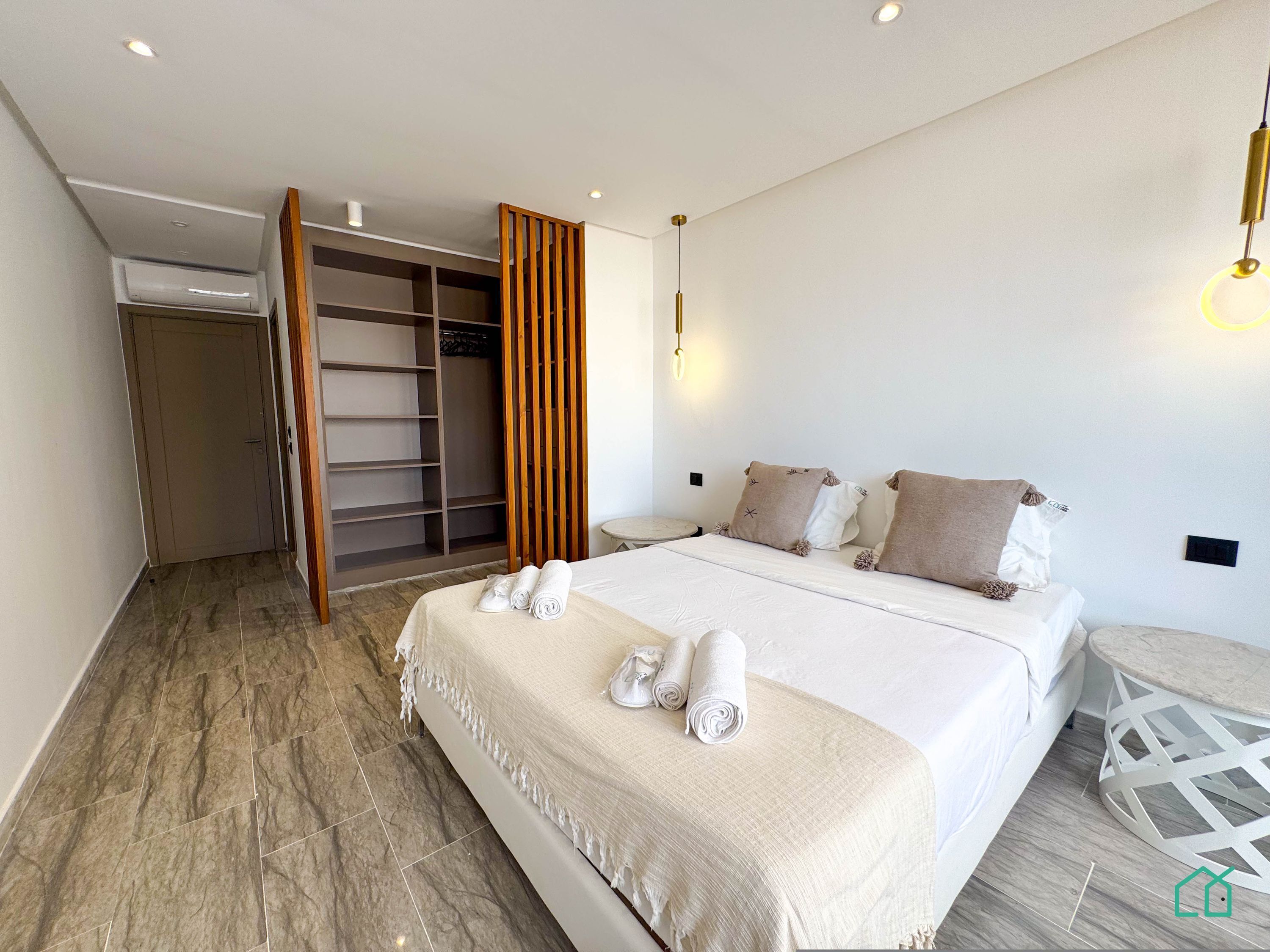 A modern bedroom with a large bed, a walk-in closet, and a round side table.
