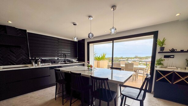 A modern kitchen with a large island, black cabinetry, and a view of the city. - The Penthouse Gammarth (La Marsa)