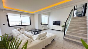 A modern living room with a sofa, a small table, and a TV. There is a staircase leading to an upper floor. - The Penthouse Gammarth (La Marsa)