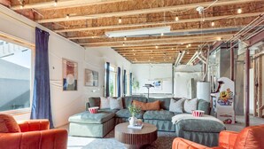 Een moderne woonkamer met een houten plafond, een groot raam met gordijnen en een zithoek met banken en een salontafel.