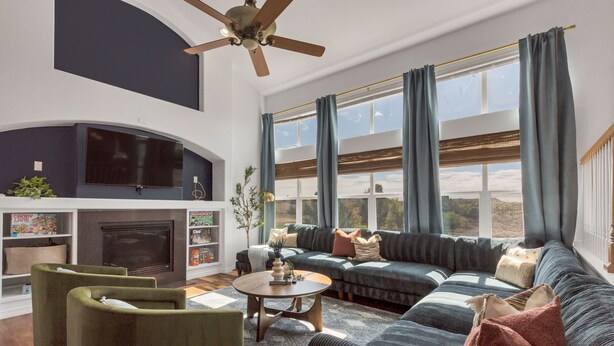 Een moderne woonkamer met een open haard, een hoekbank en een plafondventilator.