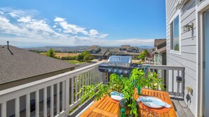 Een balkon met een barbecue, een houten tafel en uitzicht op de omgeving.