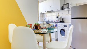 A compact kitchen with white cabinets, a microwave, a washing machine, and a glass table with chairs. - Furio Camillo Studio - Metro A - Netflix (Roma)