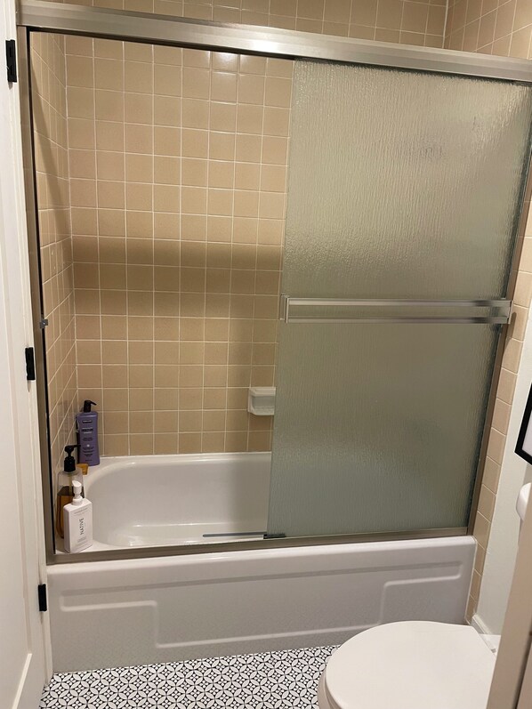 Un baño con bañera, inodoro y zona de ducha con puerta de vidrio esmerilado.