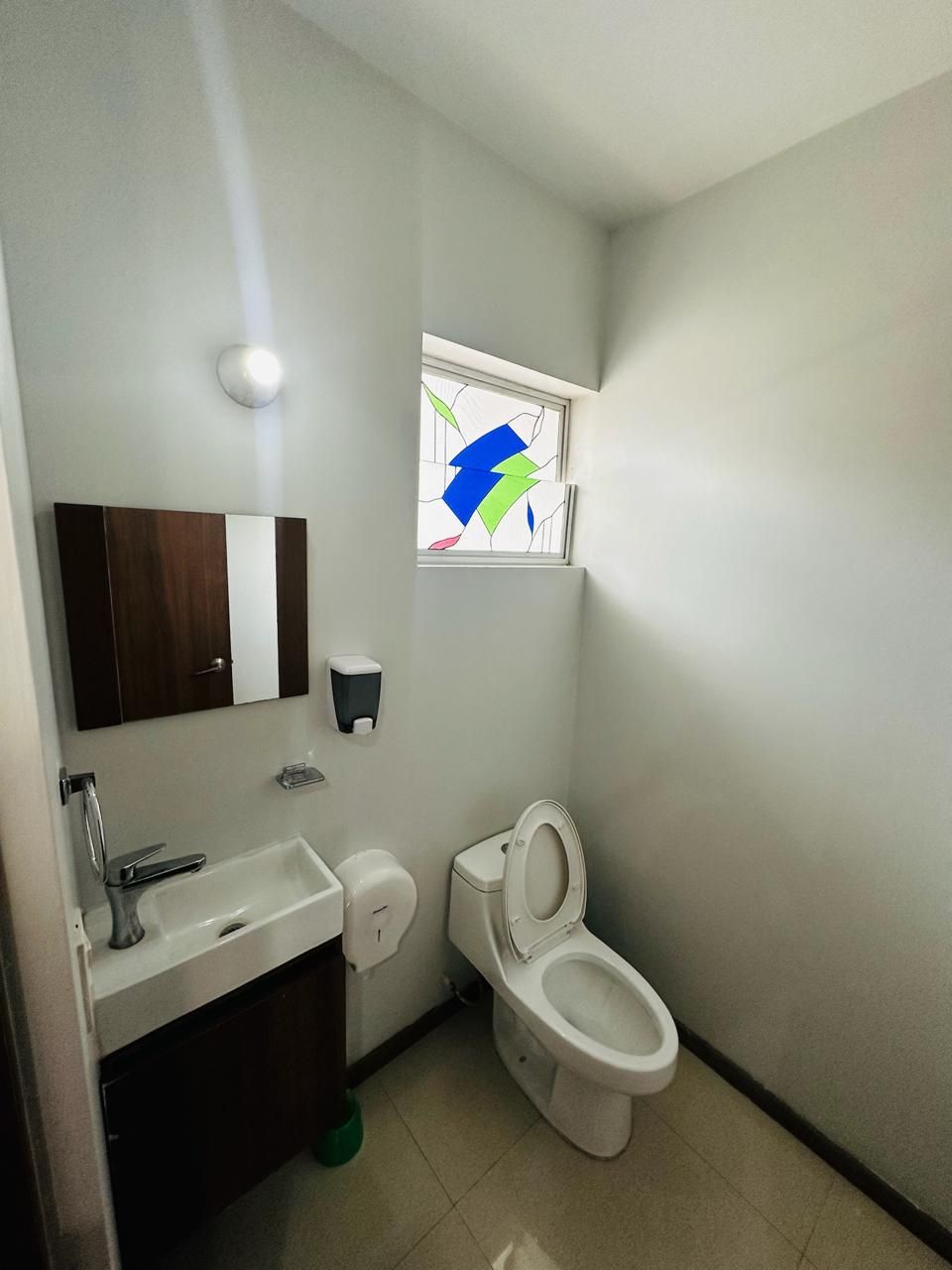 Un baño pequeño con inodoro, lavamanos y una ventana con un diseño de vitral.