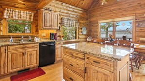 Una cocina estilo cabaña de madera con encimeras de granito, armarios de madera, lavavajillas y un comedor con un ventanal grande.
