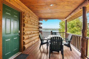 A wooden cabin with a green door, a covered porch, and a table with chairs.