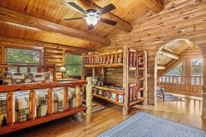 A log cabin interior with a wooden ceiling, a ceiling fan, a sofa with plaid cushions, and a wooden staircase.