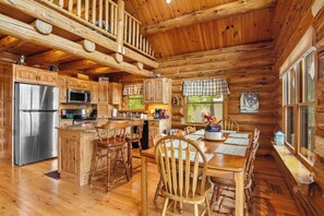 L’intérieur d’une cabane en rondins comprend une cuisine, un coin repas et une grande fenêtre.