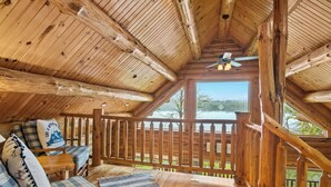 Una cabaña de madera con balcón, ventilador de techo y vista al lago.