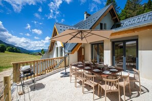 Zona pranzo con tavolo apparecchiato per quattro, posti a sedere all'aperto, barbecue e vista panoramica sulle montagne.