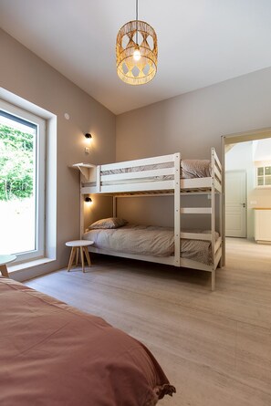 Une chambre avec un lit superposé, une fenêtre, une petite table et un luminaire suspendu.