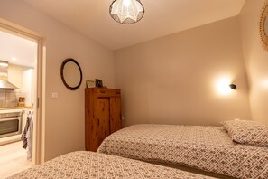 A bedroom with two beds, a wooden wardrobe, a round mirror, and a kitchen visible through an open door. - Gîte with panoramic view of the Vercors plateau (Autrans-Méaudre en Vercors)