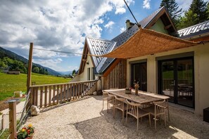 Un chalet doté d’une terrasse en bois, d’un espace salon extérieur et offrant une vue sur les montagnes.
