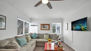 Una sala de estar con un sofá modular, una mesa de centro, un ventilador de techo y una televisión con vistas a la ciudad.