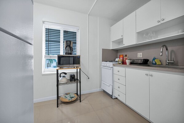 A compact kitchen with white cabinets, a microwave, a stove, and a small window with blinds.