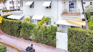 Un edificio blanco de dos pisos con un balcón, una entrada con portón y un coche amarillo estacionado adelante.