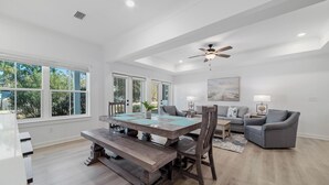 A spacious dining area with a wooden table and benches, a ceiling fan, and large windows offering a view of the outdoors. - Bayside Bliss of Orange Beach | Outdoor Pool, Kayak Launch | Dog-Friendly | My Beach Getaways (Orange Beach)