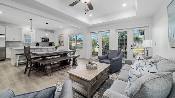A spacious living area with a dining table, gray sofas, and a ceiling fan. - Bayside Bliss of Orange Beach | Outdoor Pool, Kayak Launch | Dog-Friendly | My Beach Getaways (Orange Beach)